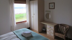 Un dormitorio con cama, escritorio, silla, armario y ventana con cortinas, con vistas al exterior.