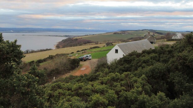 A rural landscape with a white building, a path, and a body of water in the distance.