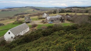 A rural landscape with a white building, a stone barn, and a blue car parked in front.