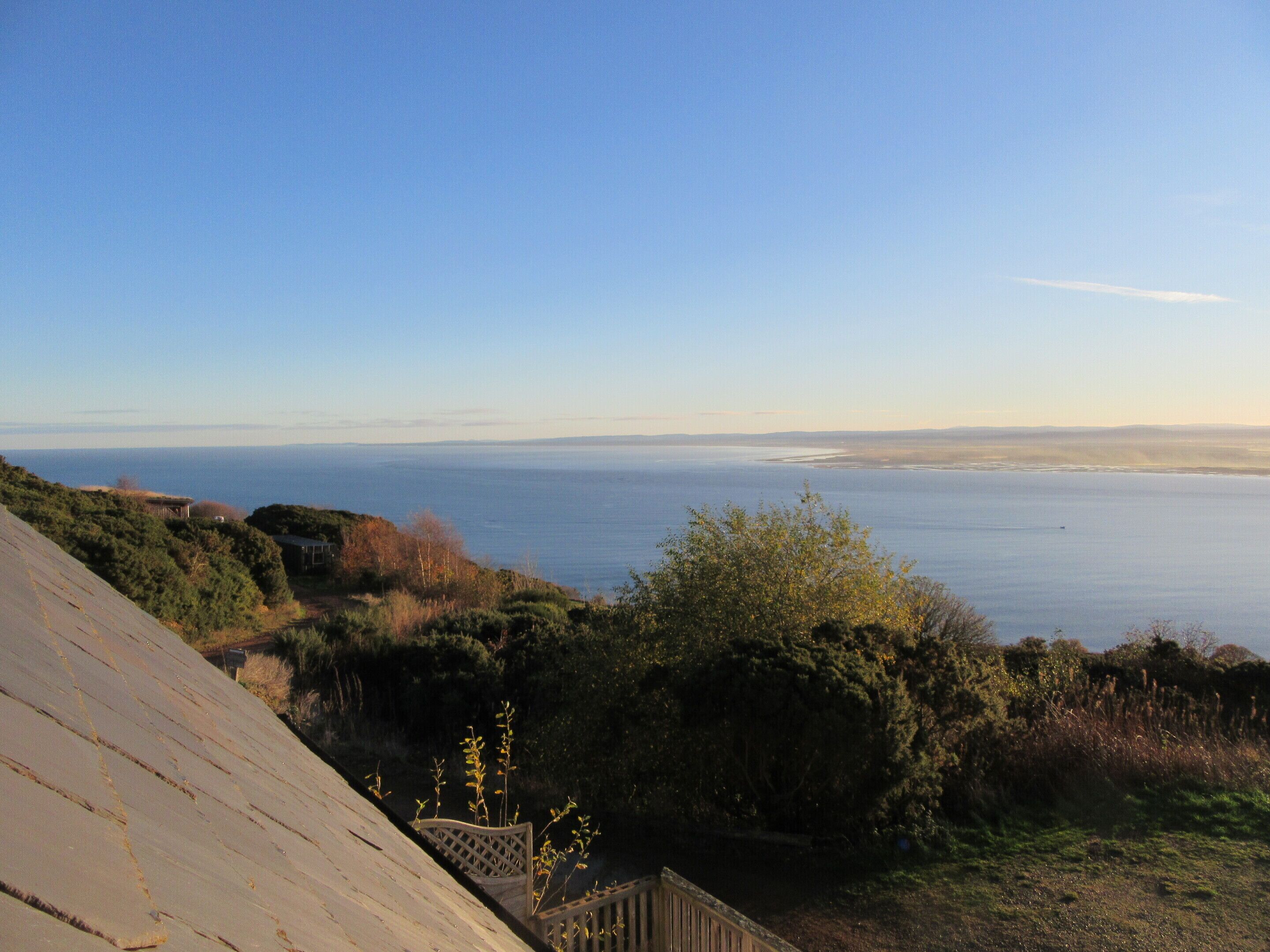 A coastal landscape with a wooden deck overlooking the sea, surrounded by vegetation.