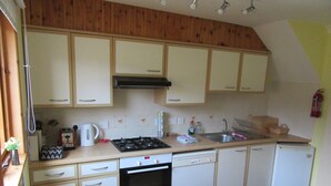 A compact kitchen with wooden cabinets, a stove, a dishwasher, and a sink. - Osprey, Longhouse Cottages (Fortrose)