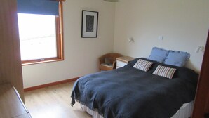 A bedroom with a bed, a window, a chair, and a desk. - Osprey, Longhouse Cottages (Fortrose)