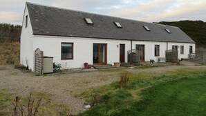 A single-story white building with a sloped roof, multiple windows, and a front door. - Osprey, Longhouse Cottages (Fortrose)
