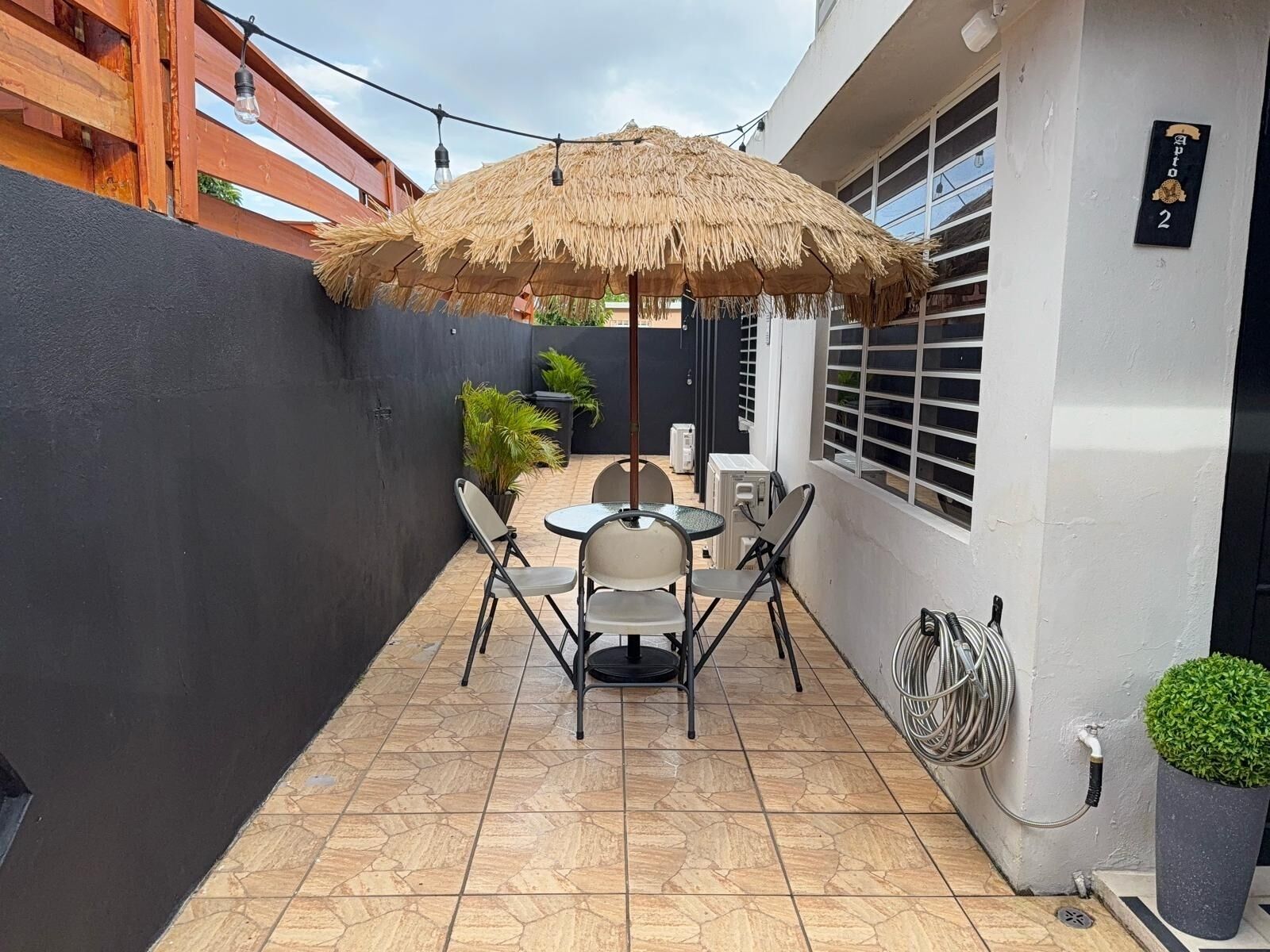 A small patio with a table and chairs, a thatched umbrella, and a potted plant.