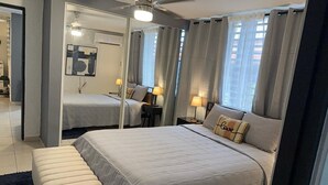 Un hotel moderno con una cama grande, un banco, un ventilador de techo y vistas a la ciudad a través de la ventana.