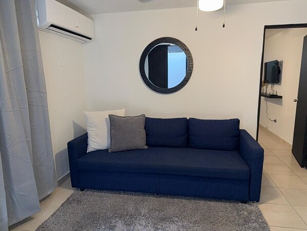 A living room with a dark blue sofa, a round mirror, and a grey rug.