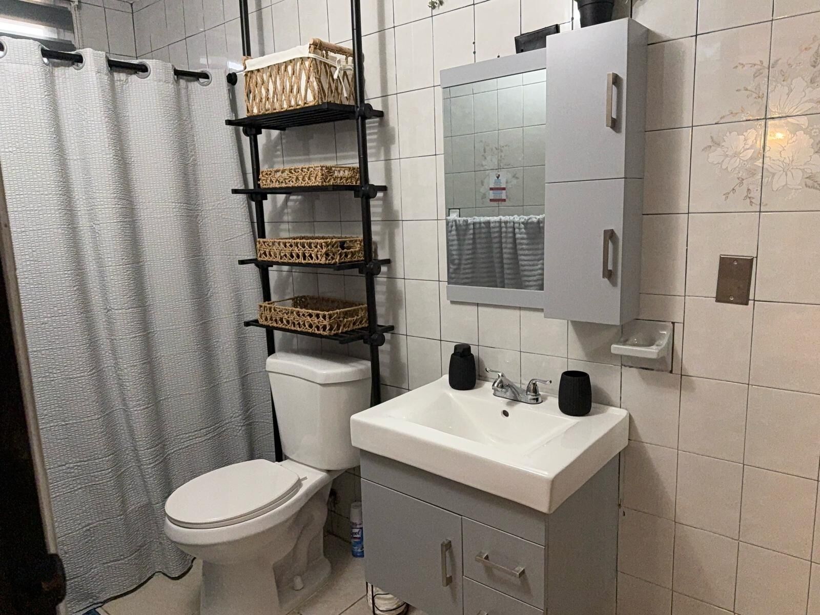 Un baño con inodoro, lavamanos, espejo y estanterías con cestas.