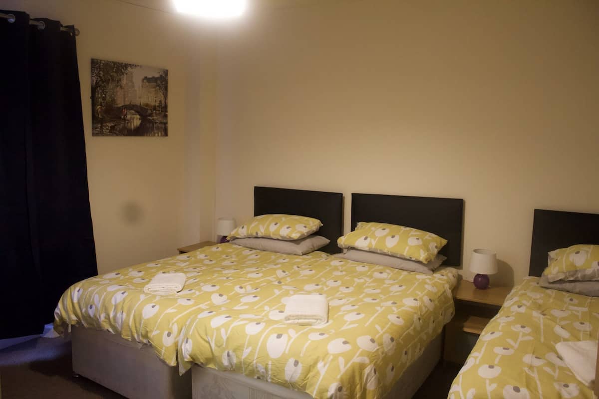 A hotel room with two beds, each with a headboard, a bedside table with a lamp, and a painting on the wall.