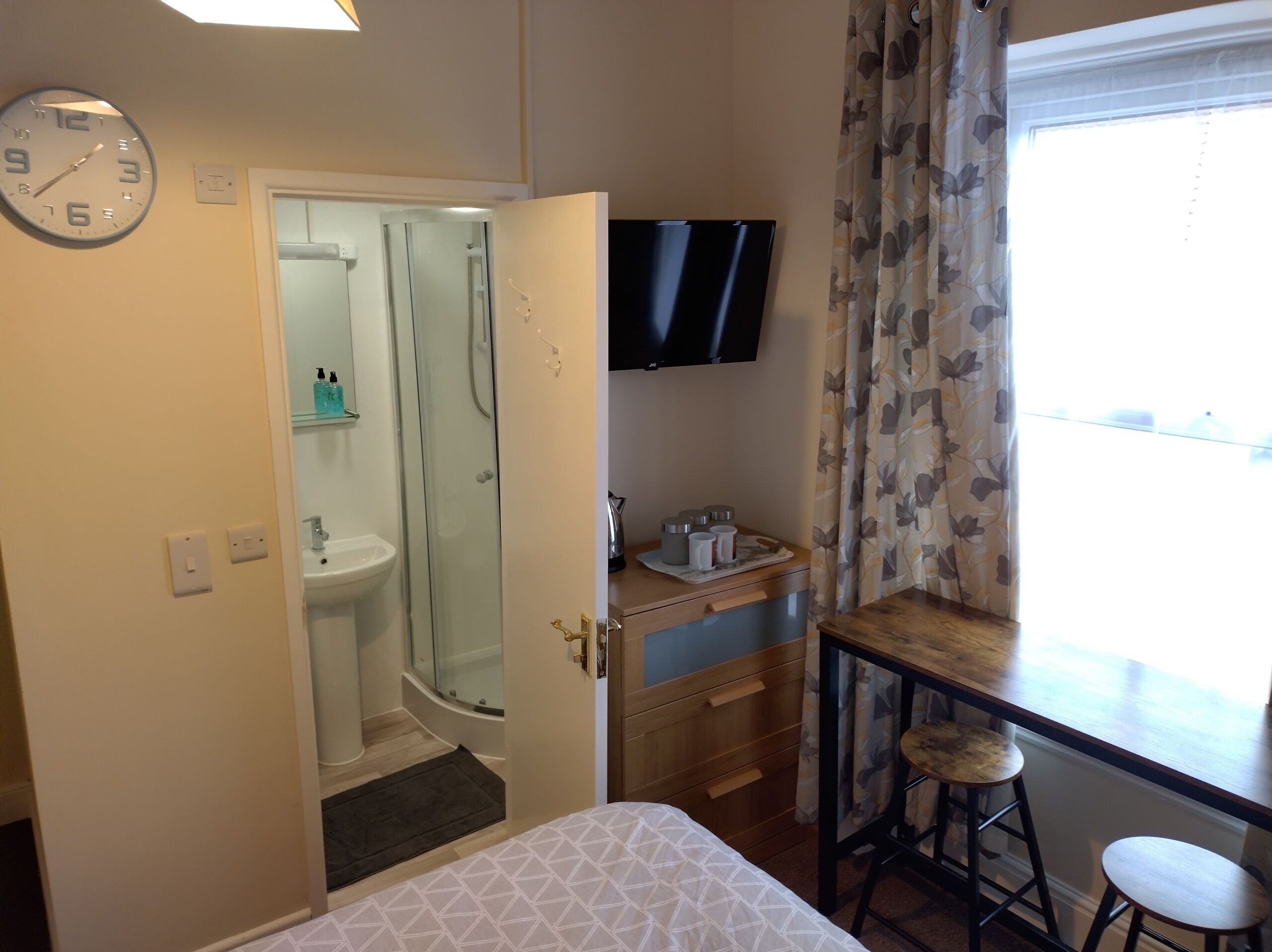 Une chambre d’hôtel avec un lit, une douche, un lavabo, une télévision et une fenêtre avec des rideaux.