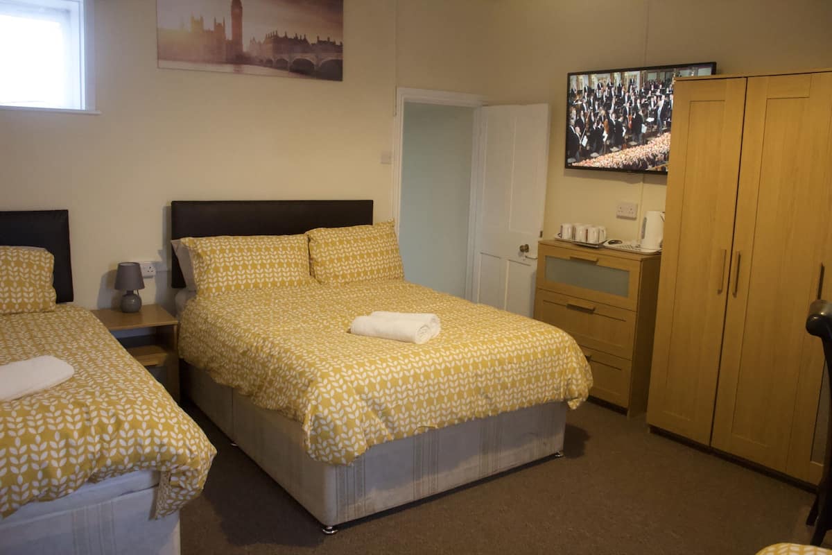 A hotel room with two beds, a television, a wardrobe, and a small table with a kettle.