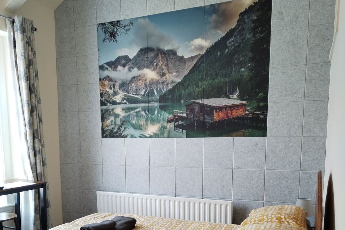 A hotel room with a bed, a nightstand, a lamp, and a large scenic wall art.