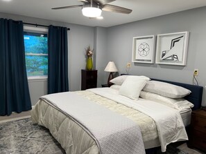 A bedroom with a bed, a nightstand, a lamp, a vase with dried flowers, and two framed pictures on the wall. - Tranquil Oasis: A Beautiful Water-Front Home (Sandwich)