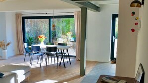 Ein modernes Wohnzimmer mit Essbereich, großen Fenstern und Blick auf Grünflächen.
