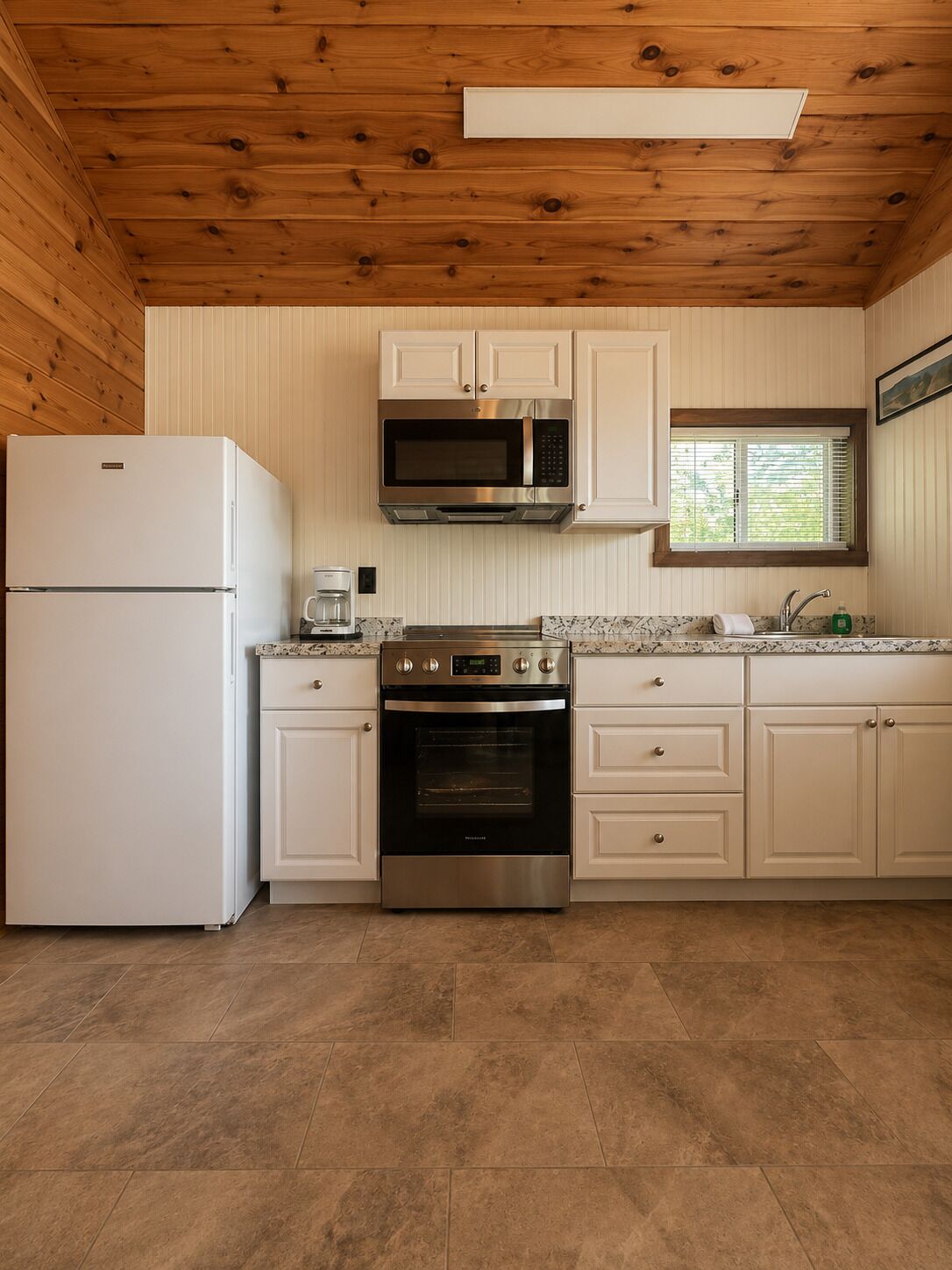A kitchen with a refrigerator, microwave, oven, and white cabinets.