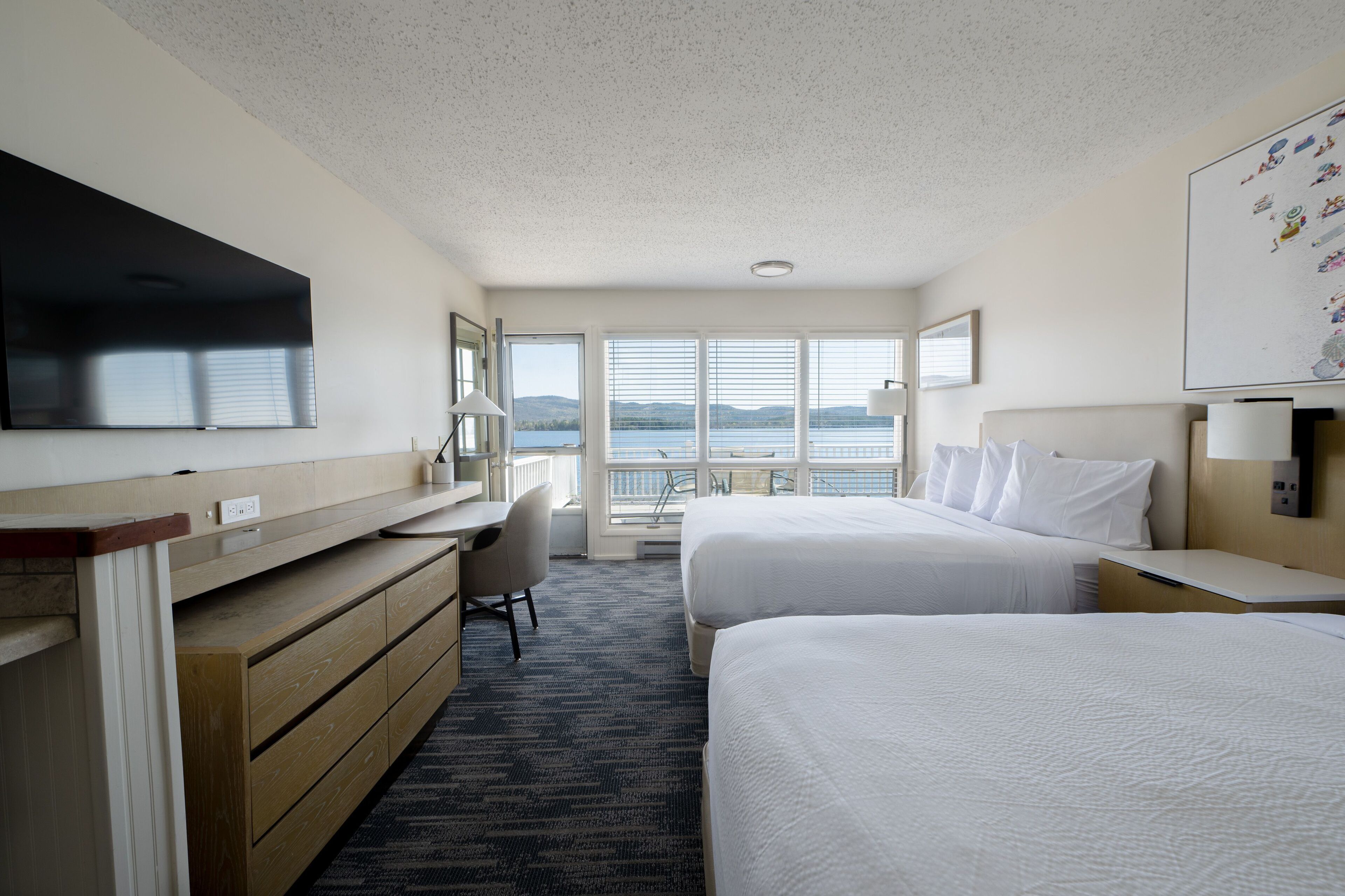 Ett hotellrum med två sängar, ett skrivbord, en stol, en TV och ett stort fönster med utsikt över havet.