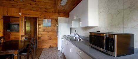 Un interior de madera con cocina, que incluye un microondas de acero inoxidable, armarios blancos y piso de baldosas.