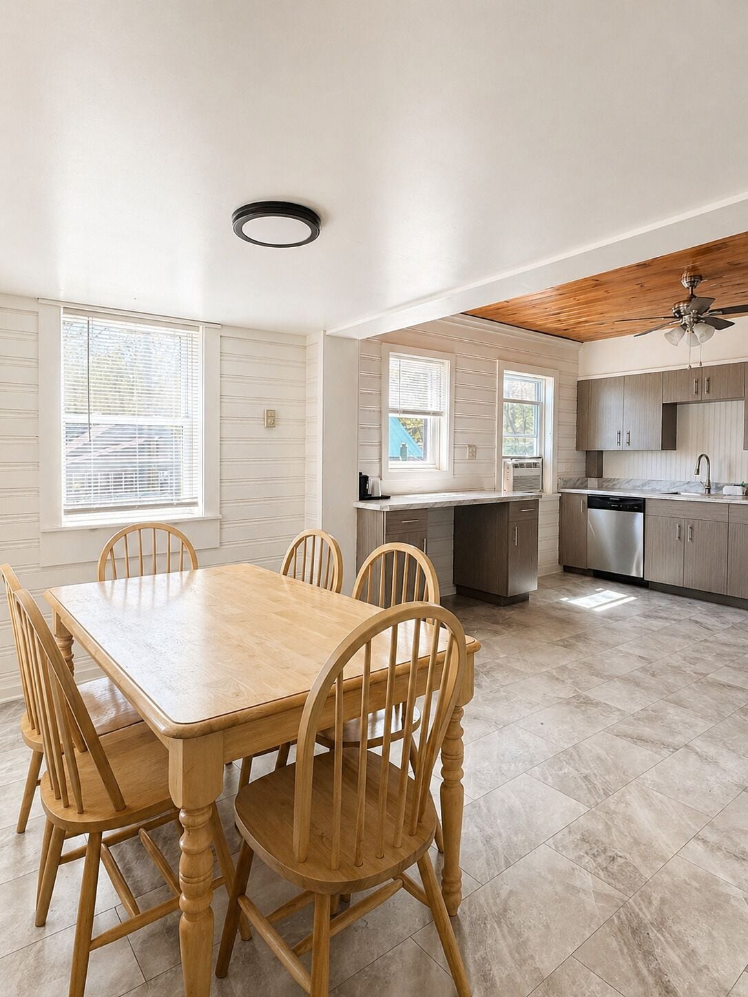 Une cuisine spacieuse avec un coin repas, des chaises en bois, un ventilateur de plafond et de grandes fenêtres.