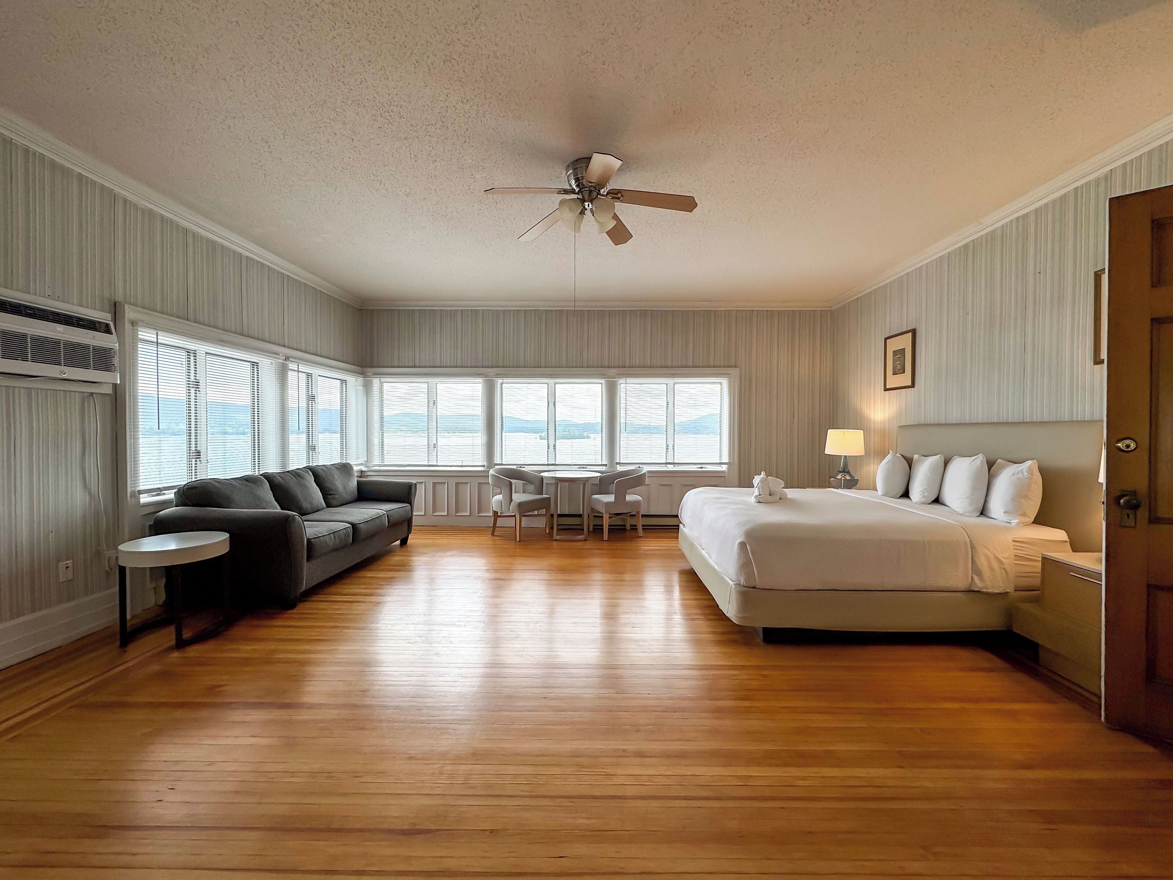 A hotel room with a large bed, a sofa, a desk, and a ceiling fan.