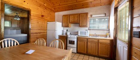L’intérieur d’une cabane en bois comprend un coin repas, une cuisine et une chambre dotée d’un ventilateur de plafond.