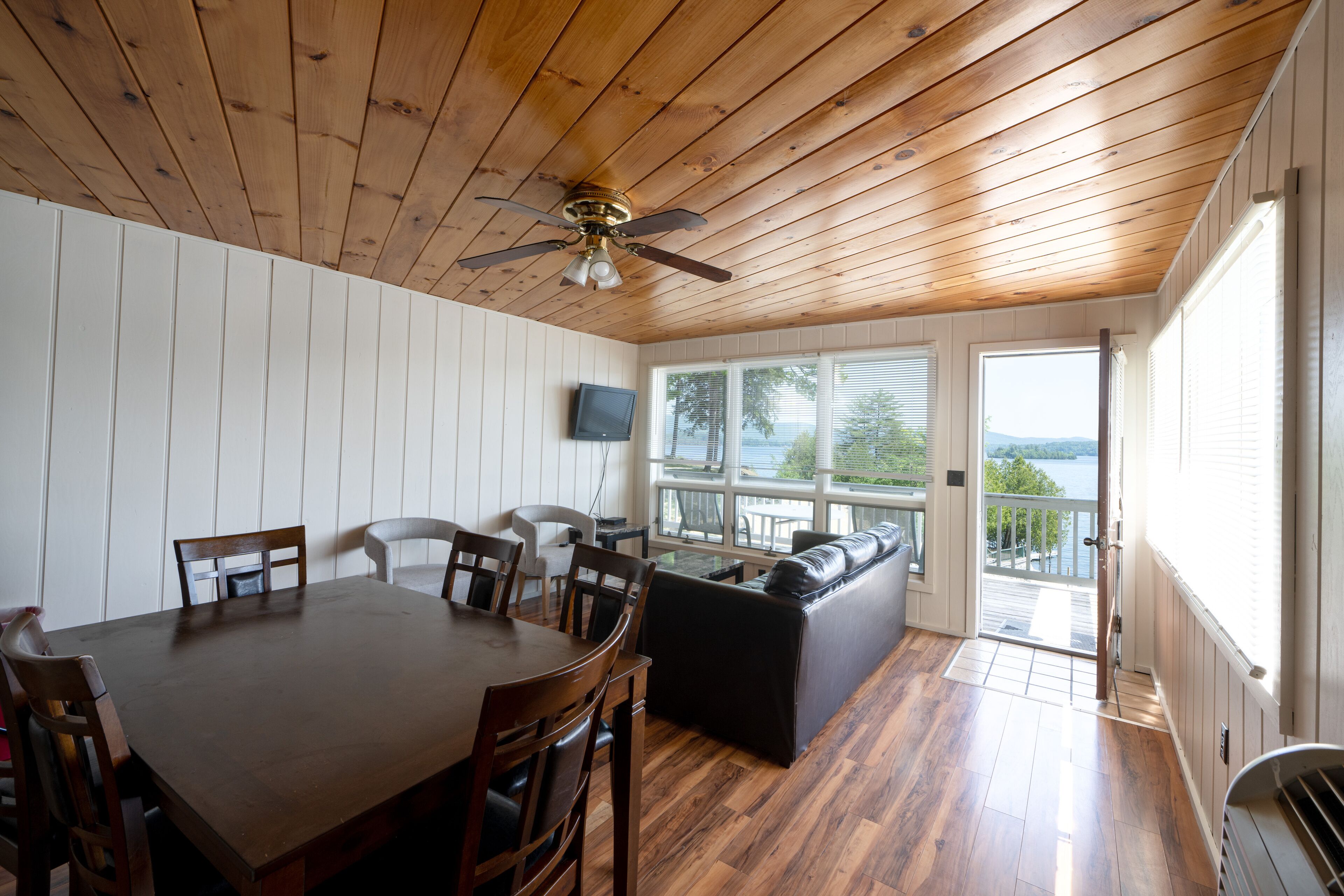 A dining area with a wooden table and chairs, a black sofa, and a ceiling fan.