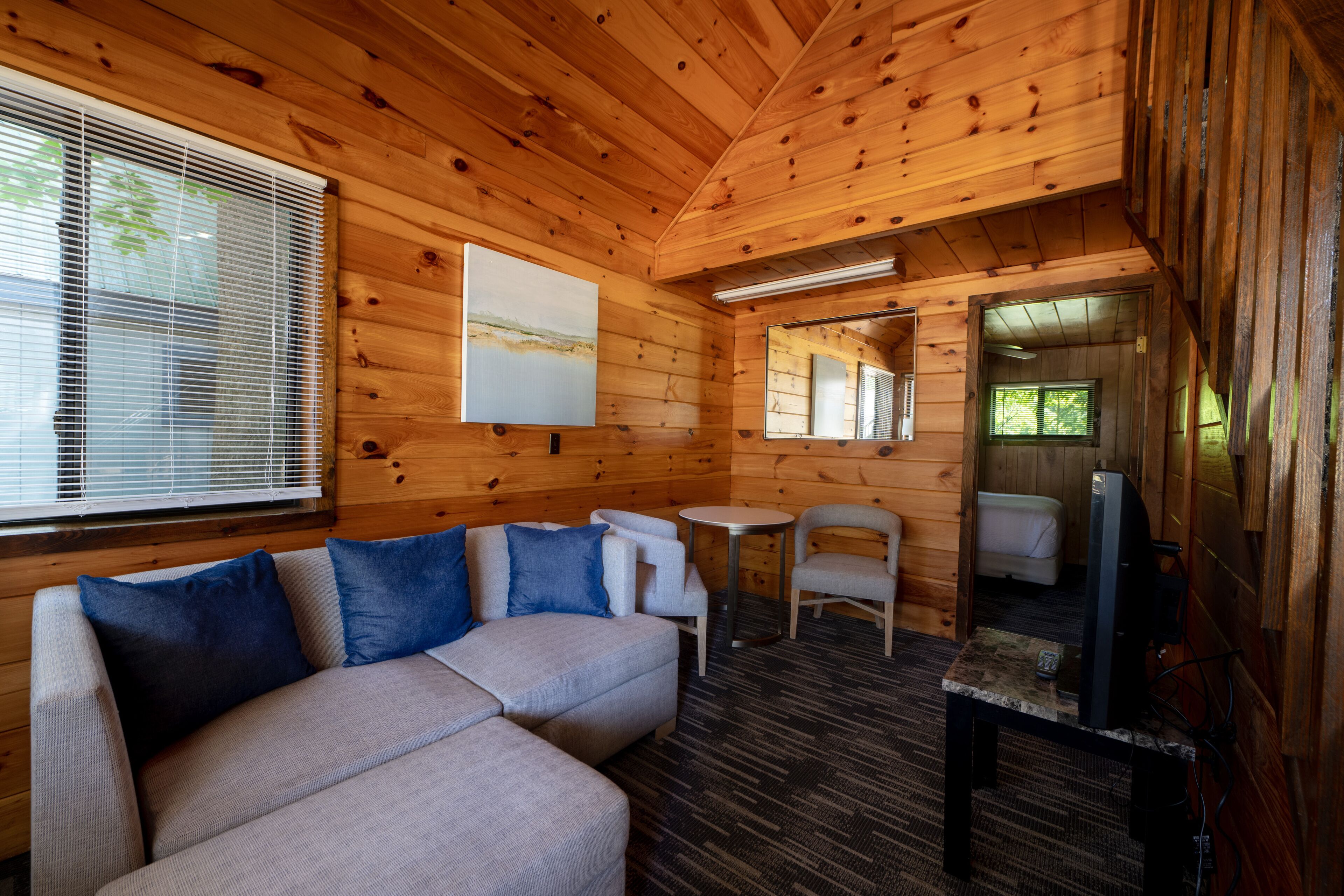 Interior de una cabaña de madera con sofá, sillas, una mesita y un televisor.