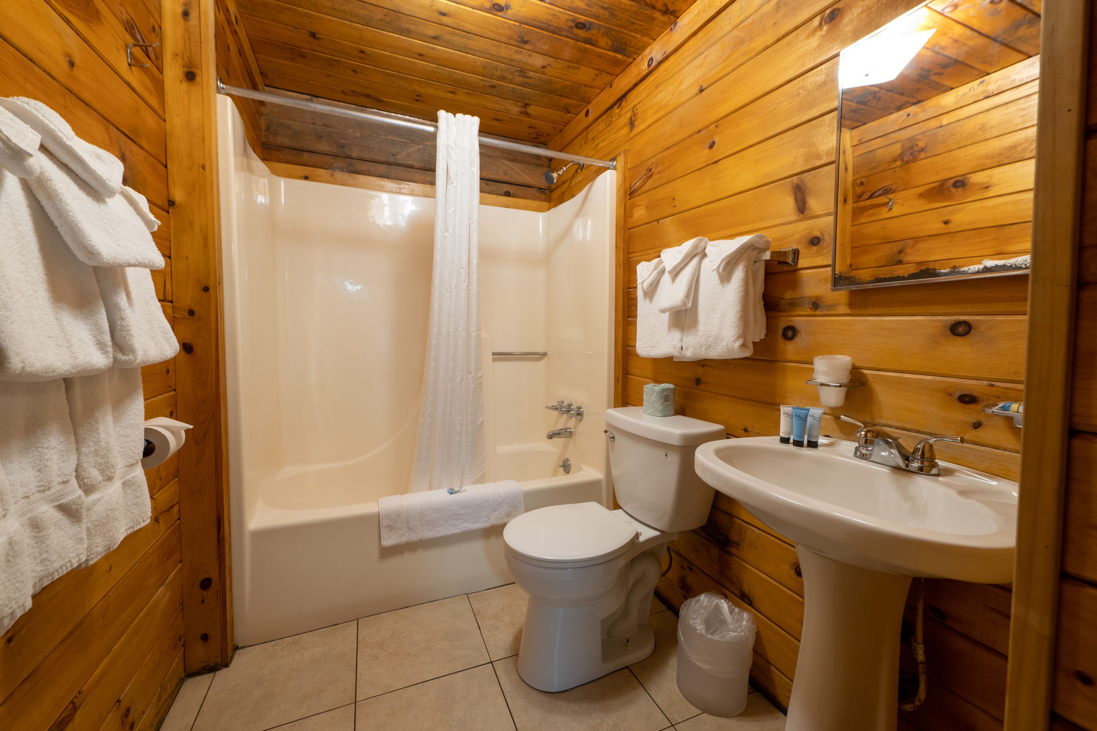 A wooden cabin bathroom with a bathtub, toilet, and sink.