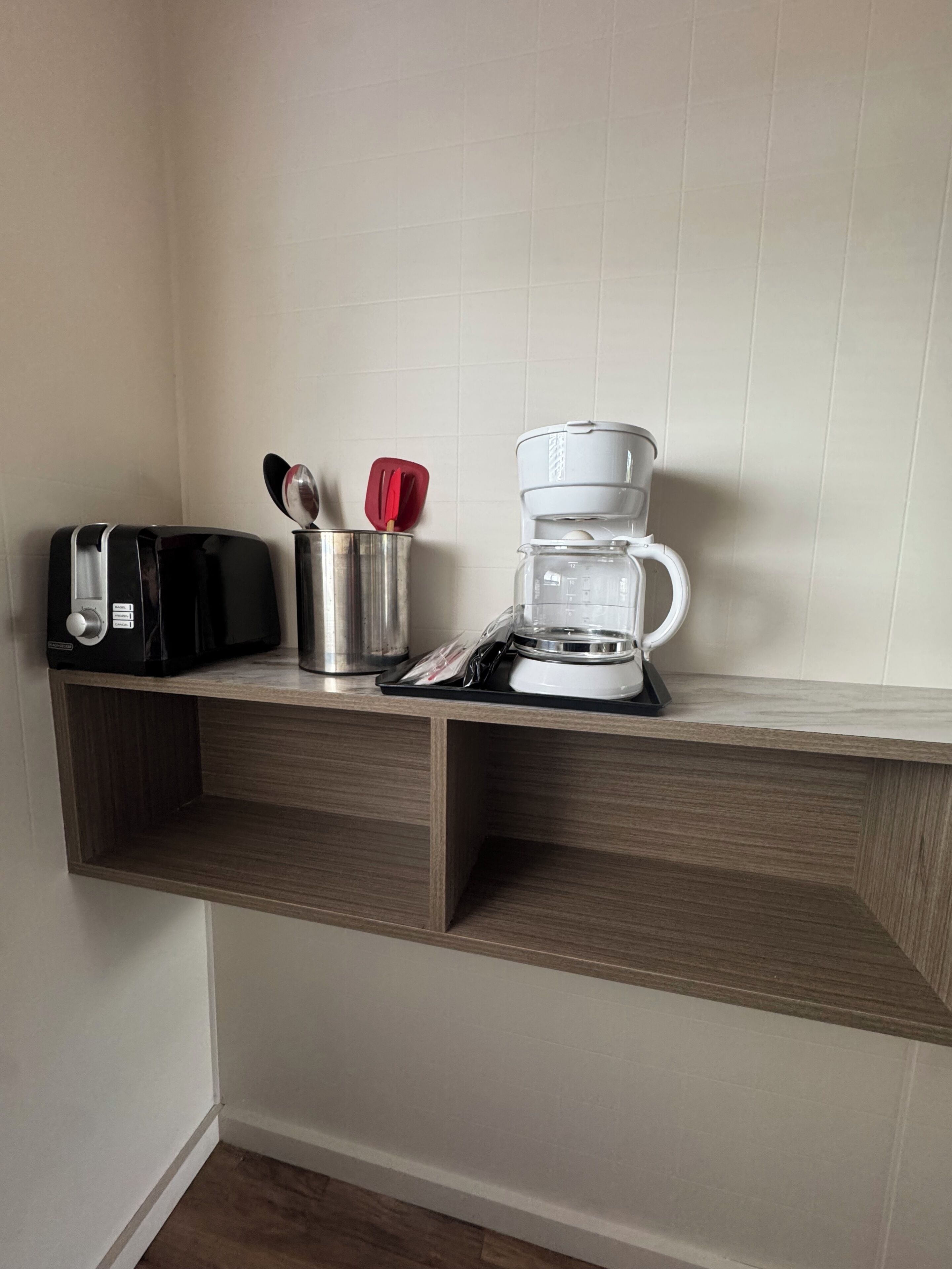 A kitchen with a coffee maker, toaster, and utensils on a wooden shelf.