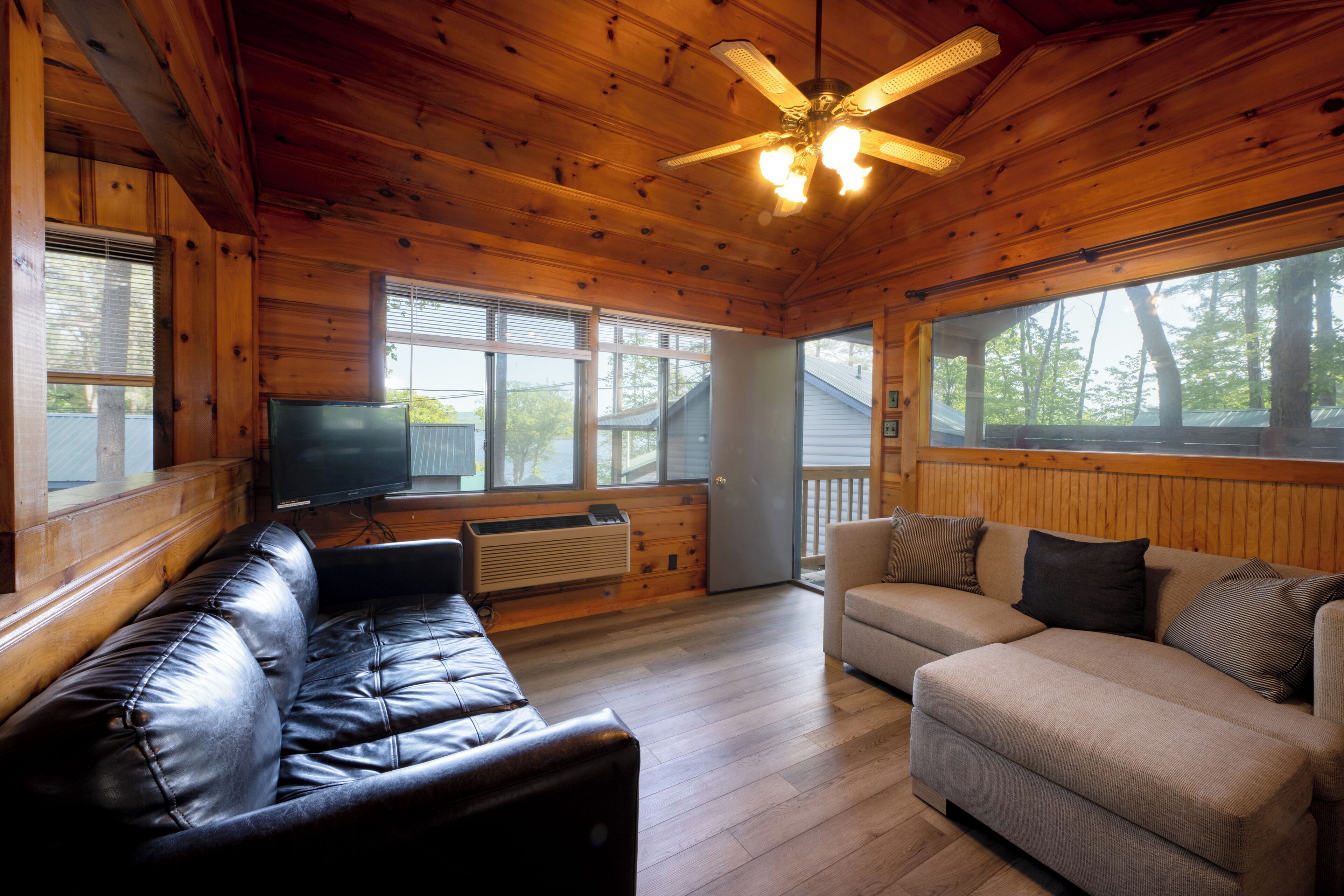 L’intérieur d’un chalet en bois, avec un canapé en cuir, un divan beige et un ventilateur de plafond.