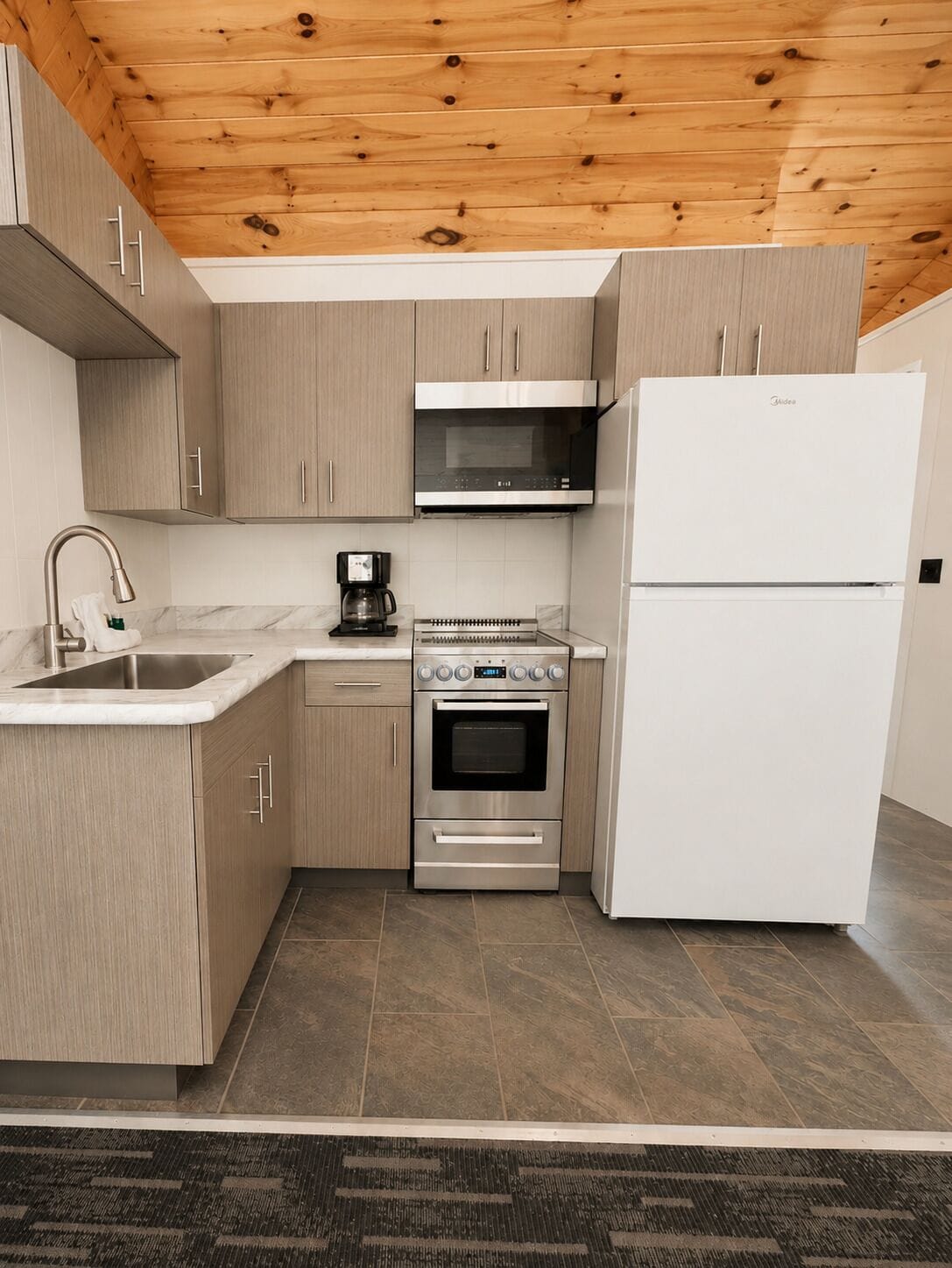 Una cocina moderna con armarios de madera clara, electrodomésticos de acero inoxidable, horno integrado y microondas.
