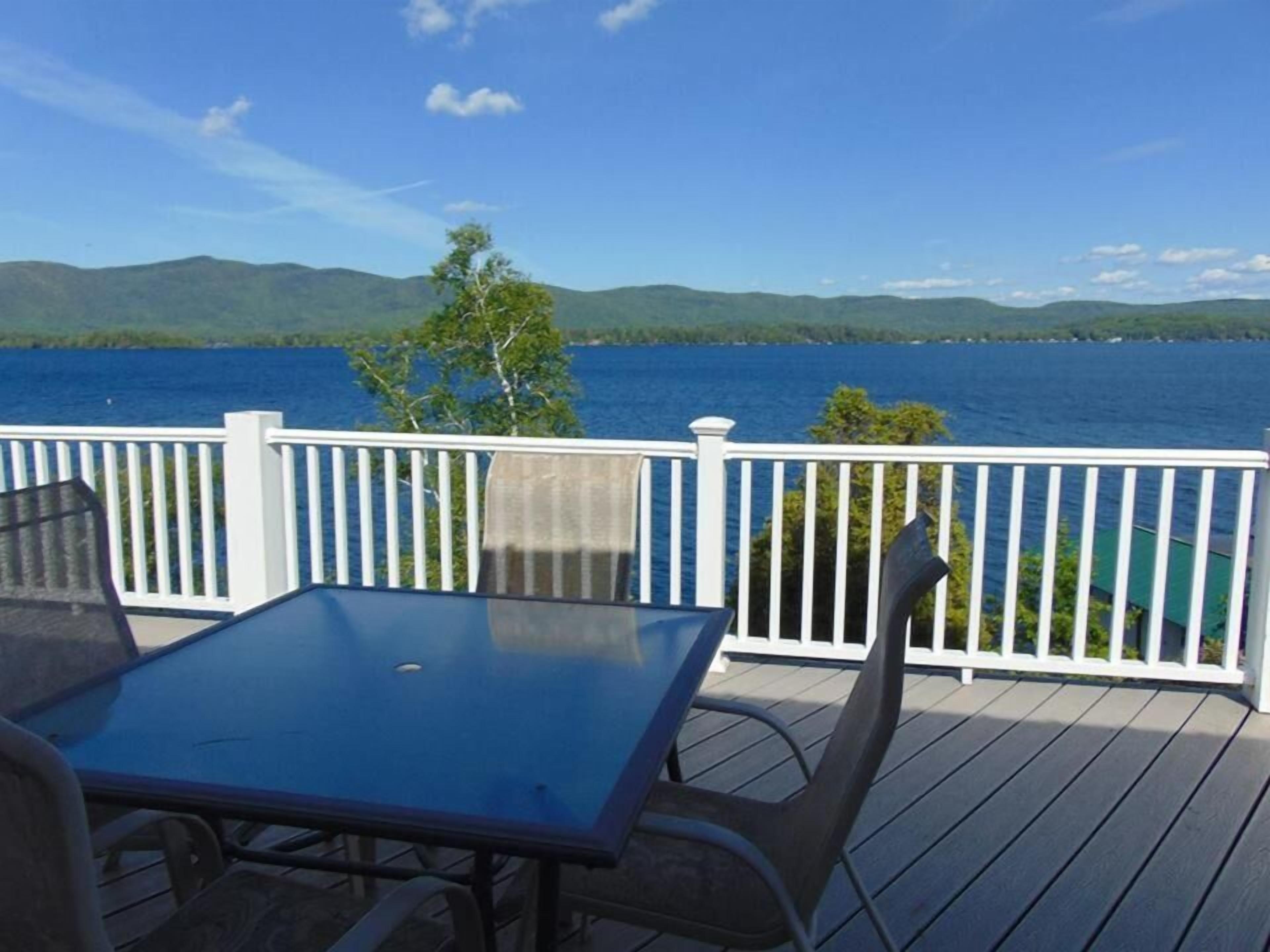 A deck with a table and chairs overlooking a lake with mountains in the background.
