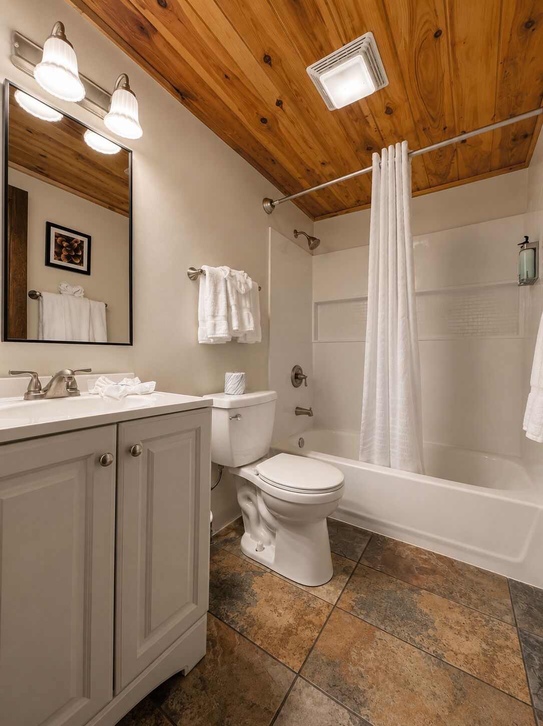 A bathroom with a wooden ceiling, a sink with a mirror, a toilet, a bathtub, and a shower curtain.