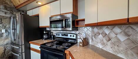 A kitchen with a stone wall, stainless steel appliances, wooden cabinets, and a tiled backsplash.