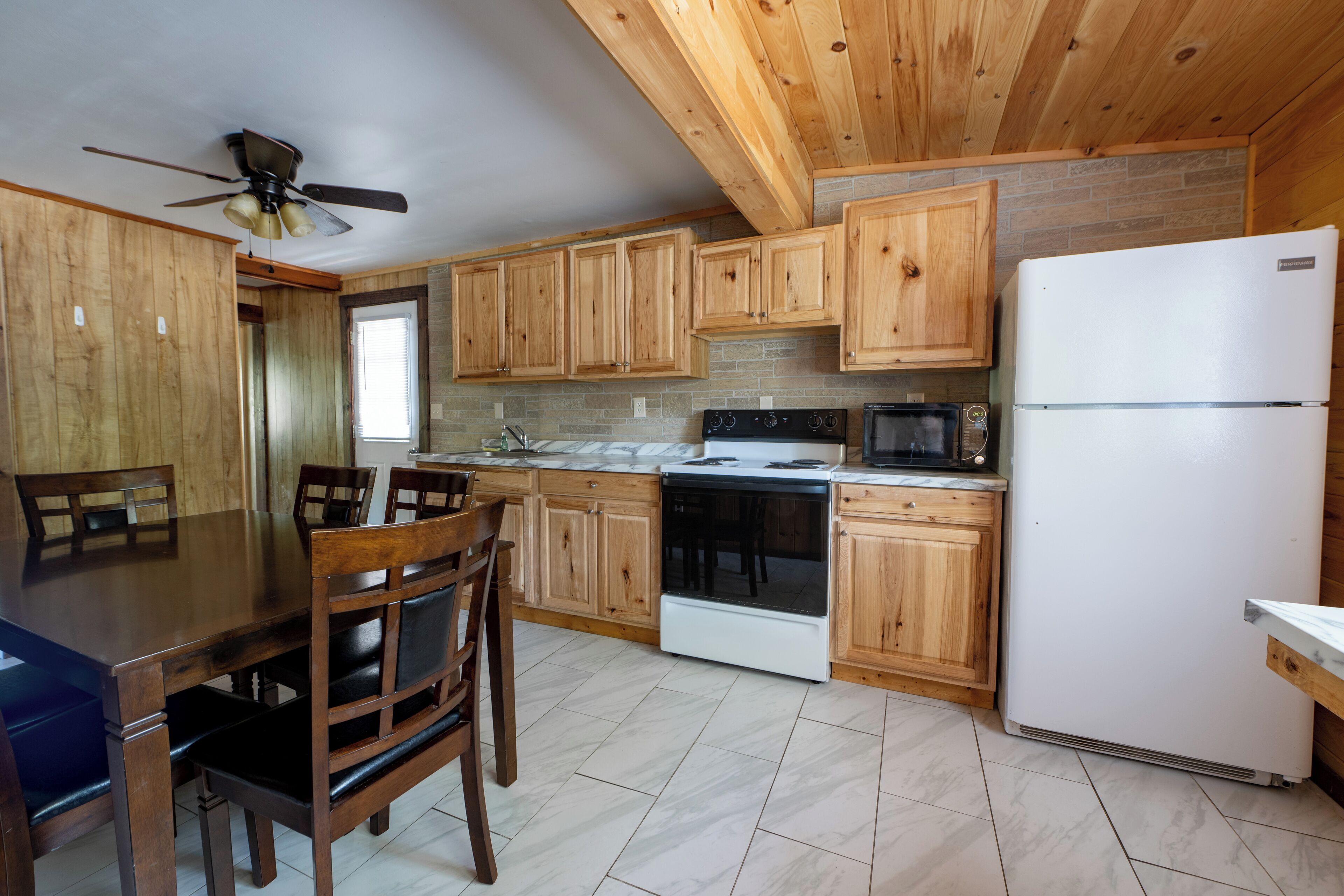 A kitchen with wooden cabinets, a white refrigerator, a stove, and a ceiling fan.