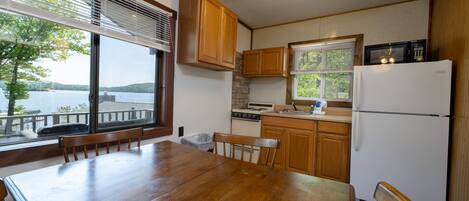 A kitchen with wooden cabinets, a stove, a microwave, and a refrigerator. There is a dining table with chairs and a window with blinds.