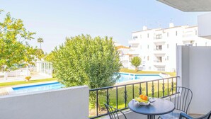 A balcony with a table and chairs, overlooking a swimming pool and a building with balconies.