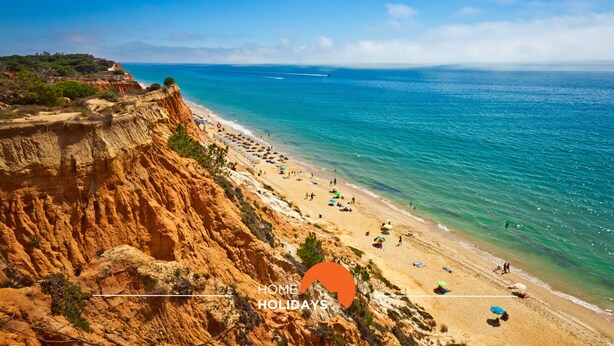 A coastal beach with clear blue waters, sandy shore, and rocky cliffs.