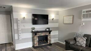 Una sala de estar moderna con chimenea de piedra, televisor montado y un rincón de asientos acogedor.