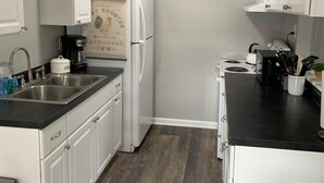 Cocina compacta con gabinetes blancos, encimera negra, pileta de acero inoxidable, refrigerador y estufa.