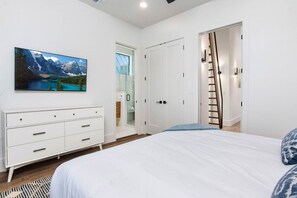 Un dormitorio con cama, cómoda, un cuadro de un paisaje montañoso y un armario con una escalera.