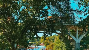 A river with numerous boats and people, surrounded by trees and a bridge.