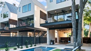A modern multi-story house with a swimming pool, outdoor seating, and a tree.