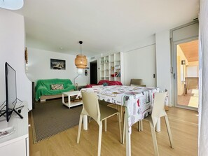 A modern living room with a dining table, chairs, a green sofa, and a bookshelf.