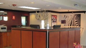 A reception desk with a wooden finish, a vase with branches, and a zebra mural on the wall. - The Teale (Kissimmee)