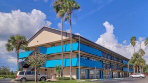 A multi-story motel with blue awnings and palm trees. - The Teale (Kissimmee)