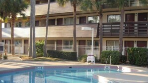 A swimming pool with a metal ladder, surrounded by a fence, and adjacent to a multi-story building with balconies. - The Teale (Kissimmee)