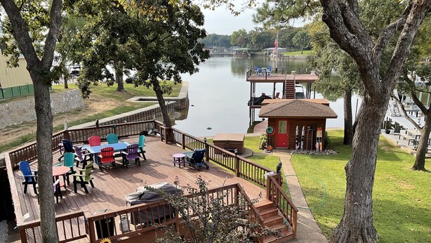 A deck with outdoor seating, a small building with a red door, and a view of a lake.