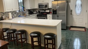 A modern kitchen with white cabinets, a stainless steel refrigerator, a microwave, and a large island with bar stools.