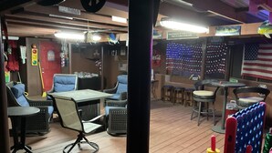 An indoor seating area with tables and chairs, a bar area with stools, and a wall decorated with lights and an American flag.