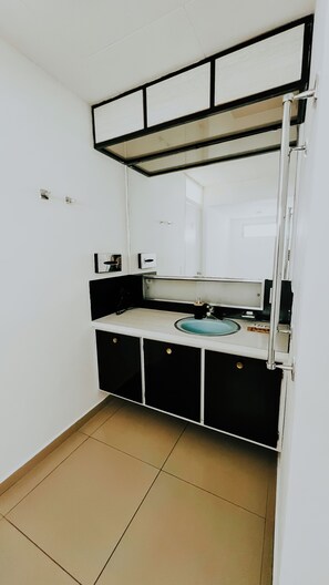 A small, compact bathroom with a white sink, black cabinets, and a mirror above the sink. - La Ruta Hotel Corporativo (San Salvador)
