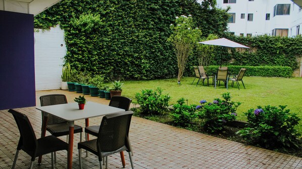 An outdoor patio with a table and chairs, surrounded by potted plants and a hedge. - La Ruta Hotel Corporativo (San Salvador)